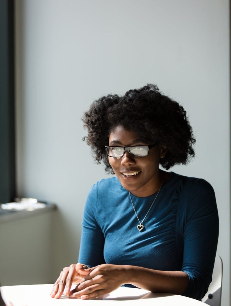 A woman in glasses smiling during a conversation at a desk.